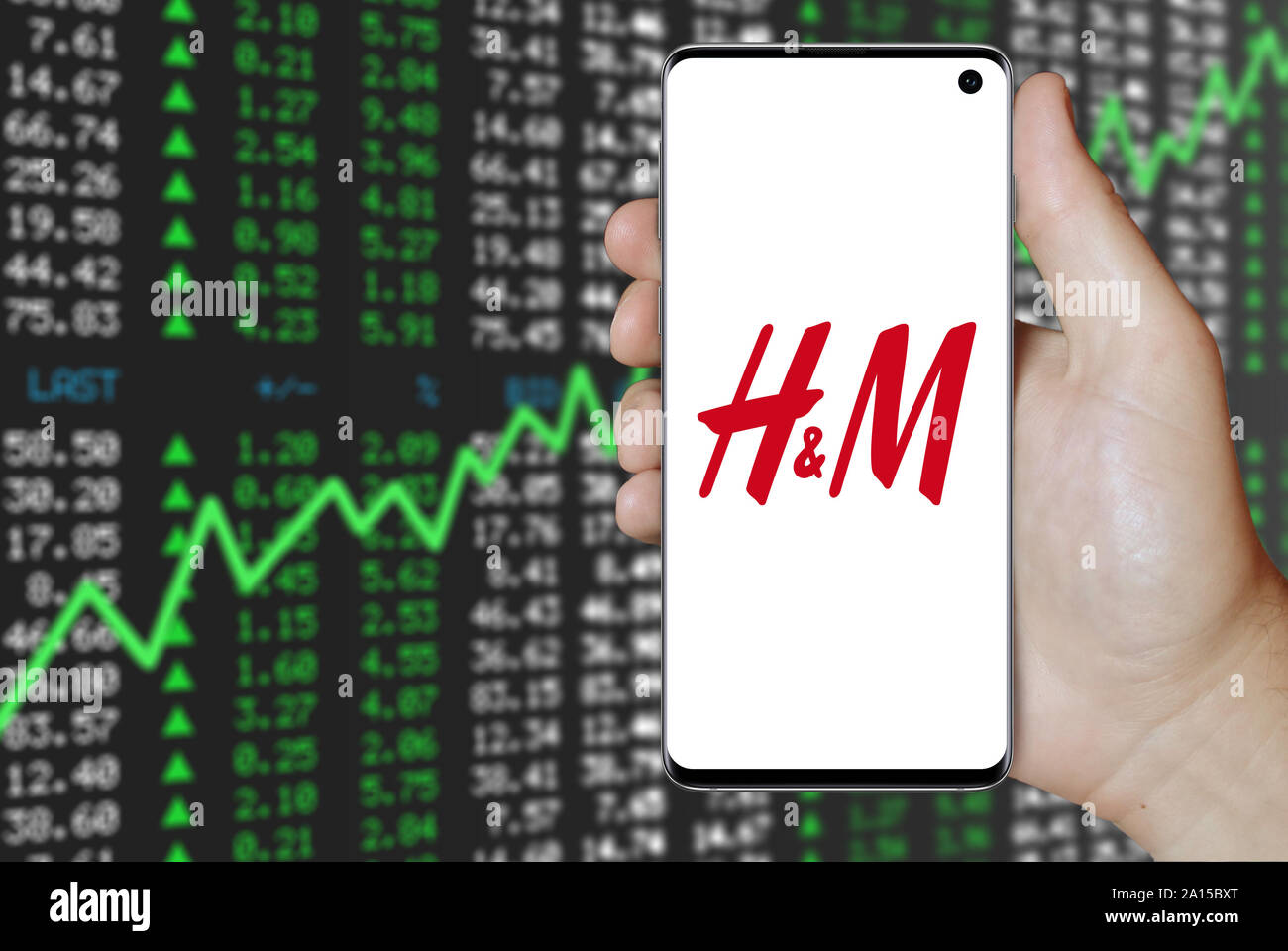 Un uomo possiede uno smartphone visualizzando il logo della società Hennes & Mauritz elencati su OMX di Stoccolma. Positivo del mercato azionario sfondo. Credito: PIXDUCE Foto Stock