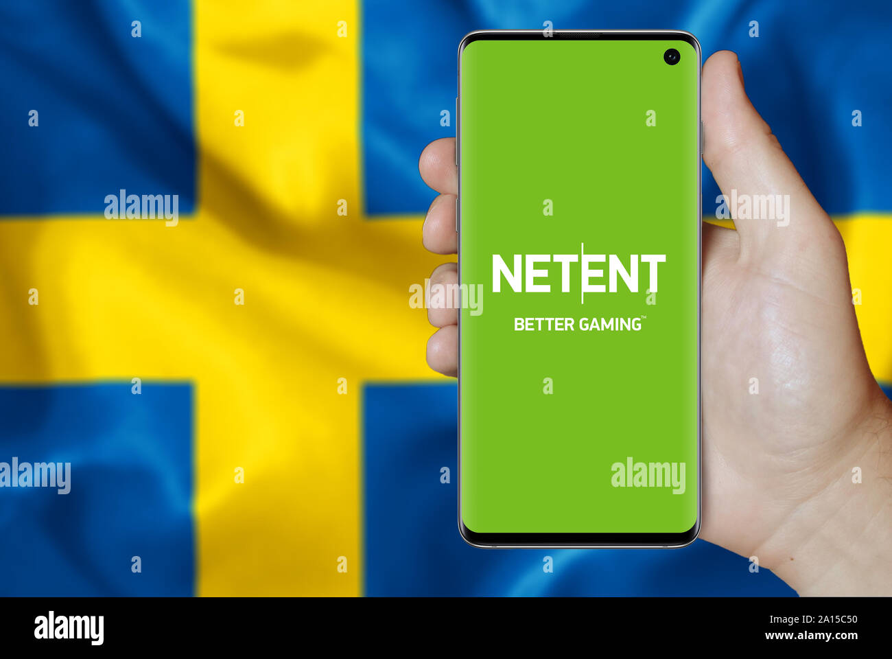 Un uomo possiede uno smartphone visualizzando il logo della società NetEnt elencati su OMX di Stoccolma. Bandiera svedese in background. Credito: PIXDUCE Foto Stock