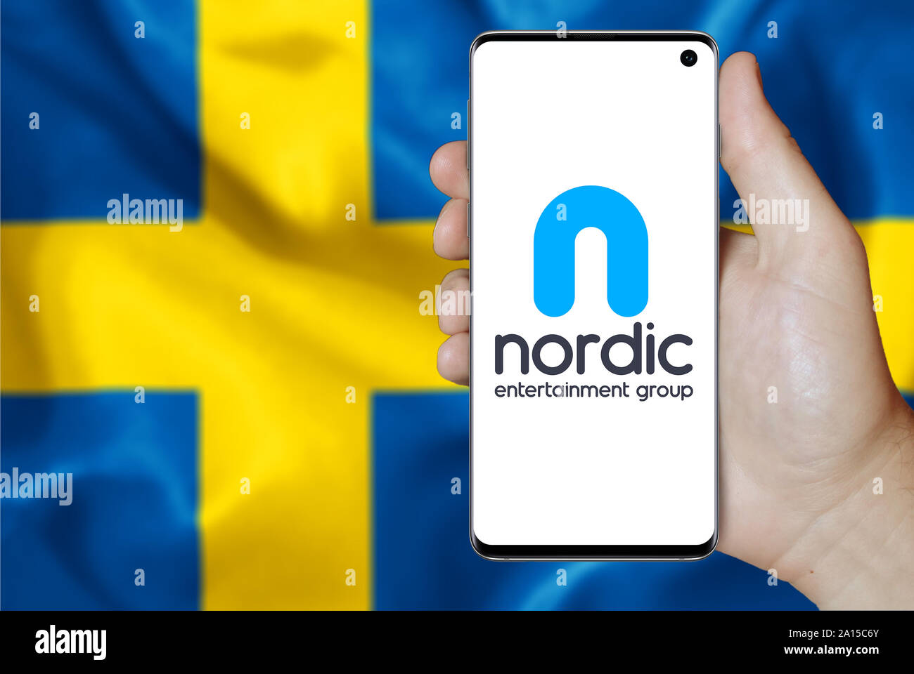 Un uomo possiede uno smartphone visualizzando il logo della società Nordic Entertainment Group elencati su OMX di Stoccolma. Bandiera svedese. Credito: PIXDUCE Foto Stock