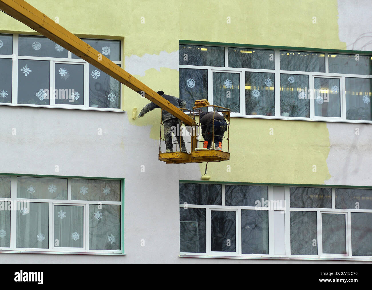 Mestiere pericoloso, pittori lavorando su gru mobile platform e vernice edificio multipiano giallo su un sordo a freddo giorno d'inverno. Foto Stock