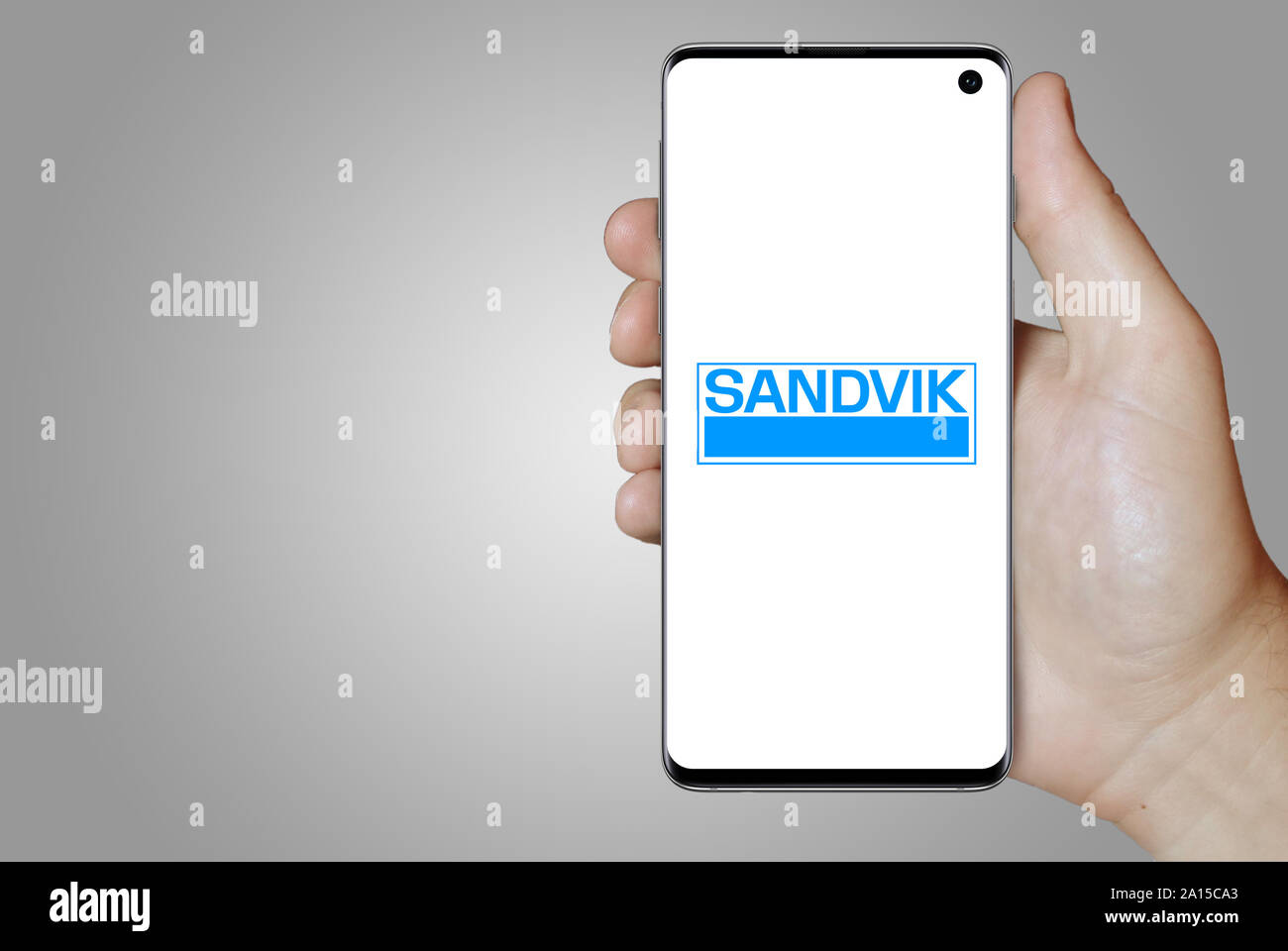 Un uomo possiede uno smartphone visualizzando il logo dell'impresa Sandvik elencati su OMX di Stoccolma. Sfumatura grigia in background. Credito: PIXDUCE Foto Stock