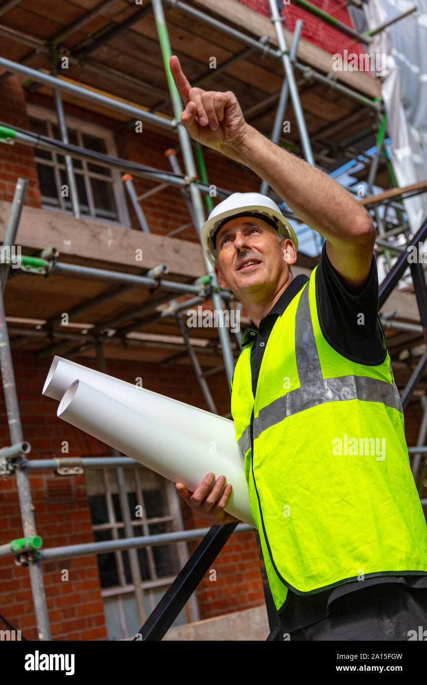 Builder maschio foreman, lavoratore geometra, ingegnere o architetto sul sito in costruzione tenendo i progetti di un edificio e puntamento Foto Stock