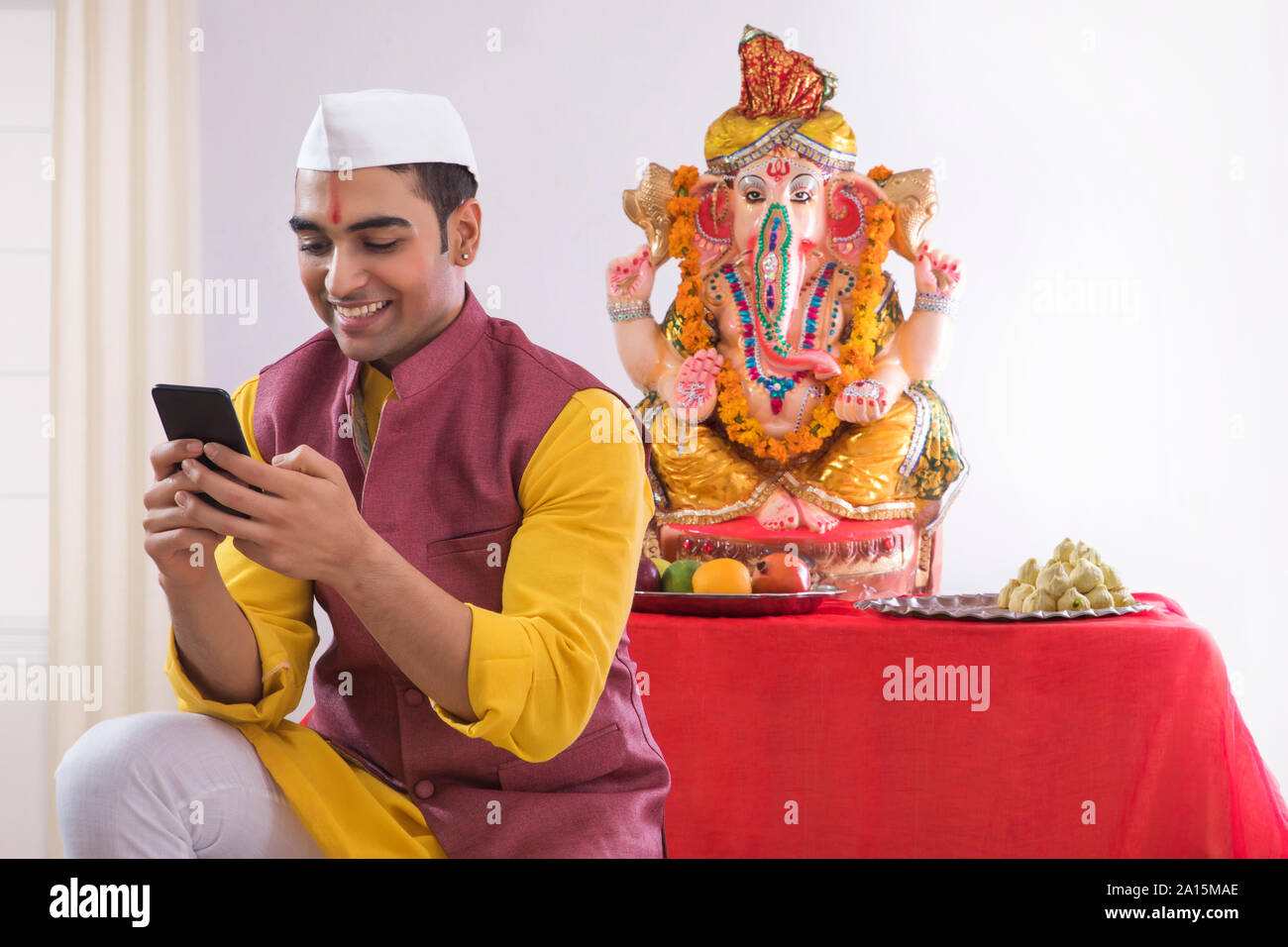 Uomo seduto di fronte a Ganesh idolo utilizzando il telefono cellulare Foto Stock