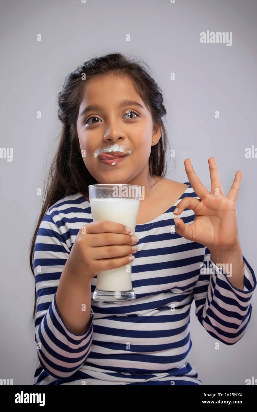 Ritratto di una ragazza sorridente con il latte di baffi tenendo un bicchiere di latte e facendo un segno OK con la mano Foto Stock