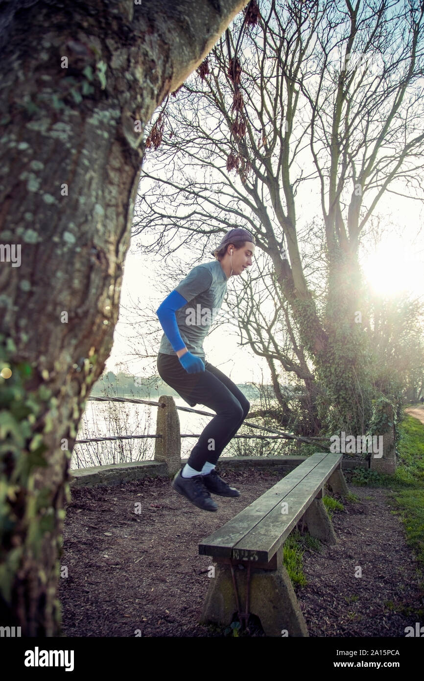 Giovane uomo sportivo saltando su una panca in legno Foto Stock