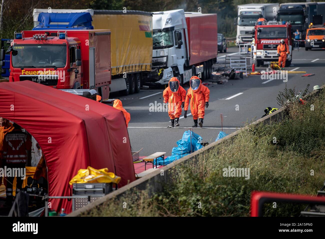 Germania. 24Sep, 2019. Due vigili del fuoco in tute di protezione a piedi passato la scena dell'incidente. Nell'incidente con quattro camion sull'autostrada 2 tra Peine e Braunschweig una sostanza pericolosa scampato. Secondo la polizia, due persone sono state gravemente ferite e un merci pericolose transporter è stato anche coinvolto. Credito: Sina Schuldt/dpa/Alamy Live News Foto Stock