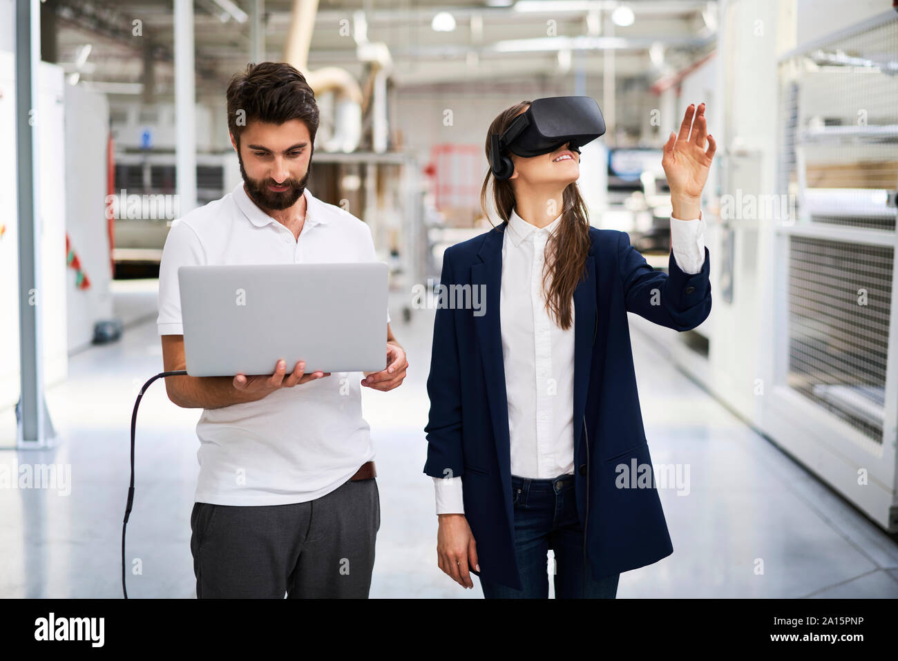 Uomo con notebook e imprenditrice indossando occhiali VR in fabbrica Foto Stock