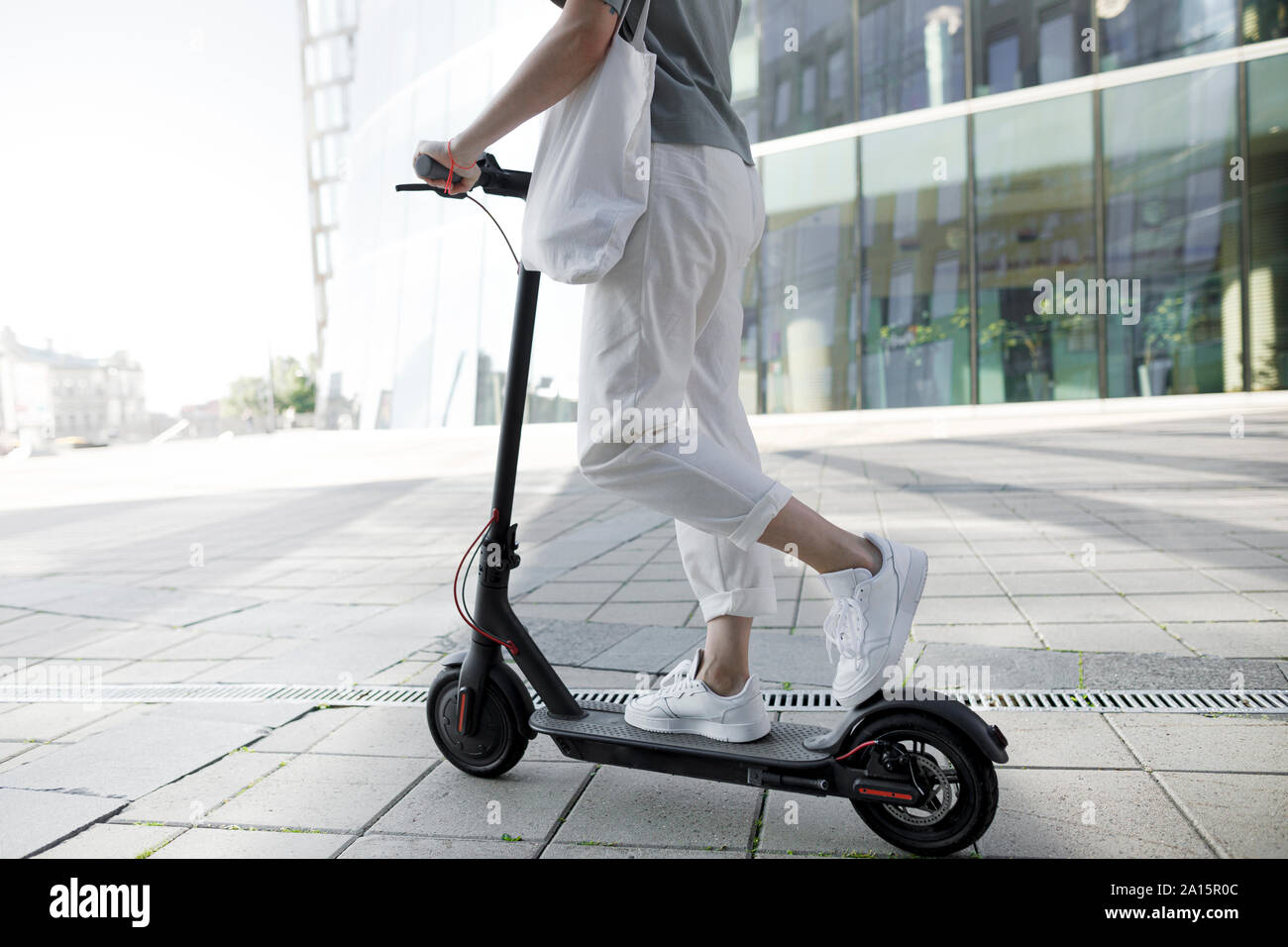 Giovane donna su e-scooter, edifici moderni in background Foto Stock