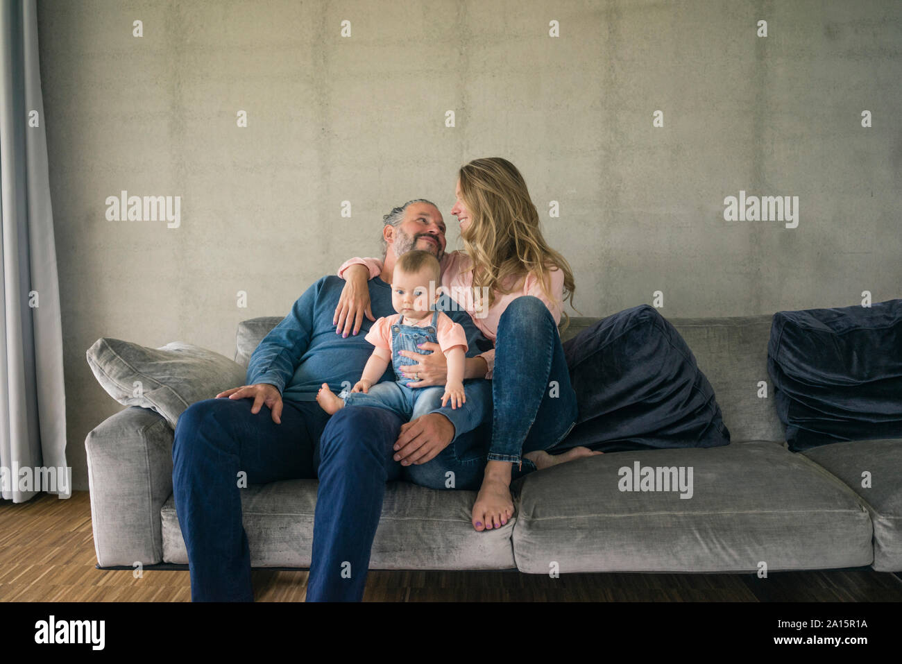 La famiglia felice di tre seduti sul divano di casa Foto Stock
