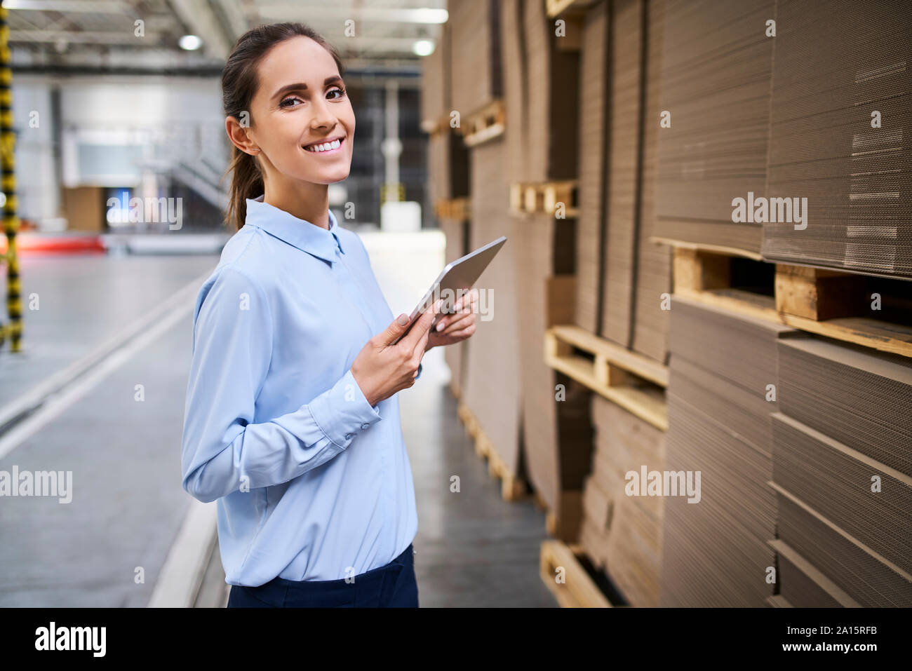 Ritratto di imprenditrice sorridente con la compressa in un magazzino di fabbrica Foto Stock