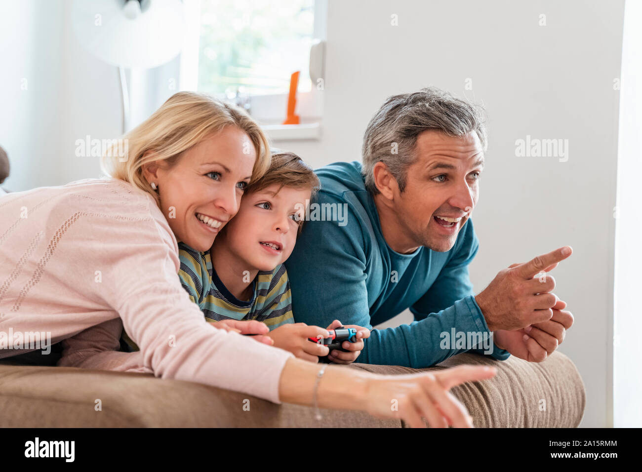 Genitori felici con il figlio la riproduzione di video gioco sul lettino a casa Foto Stock