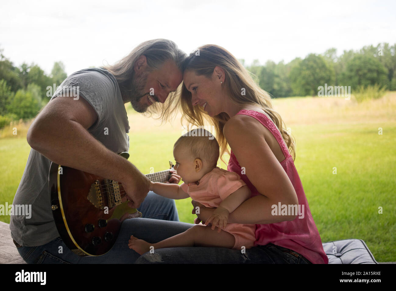 Padre, madre e bambina seduti all'aperto con la chitarra Foto Stock