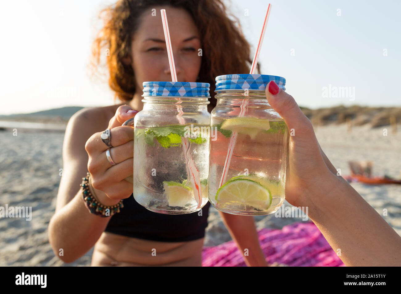 Due bicchieri con acqua, calce e menta, amici la tostatura in spiaggia Foto Stock