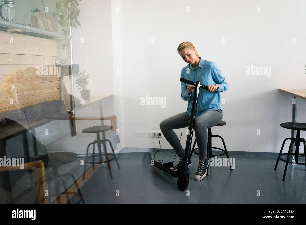 Giovane donna in carica e-scooter in coffee shop Foto Stock