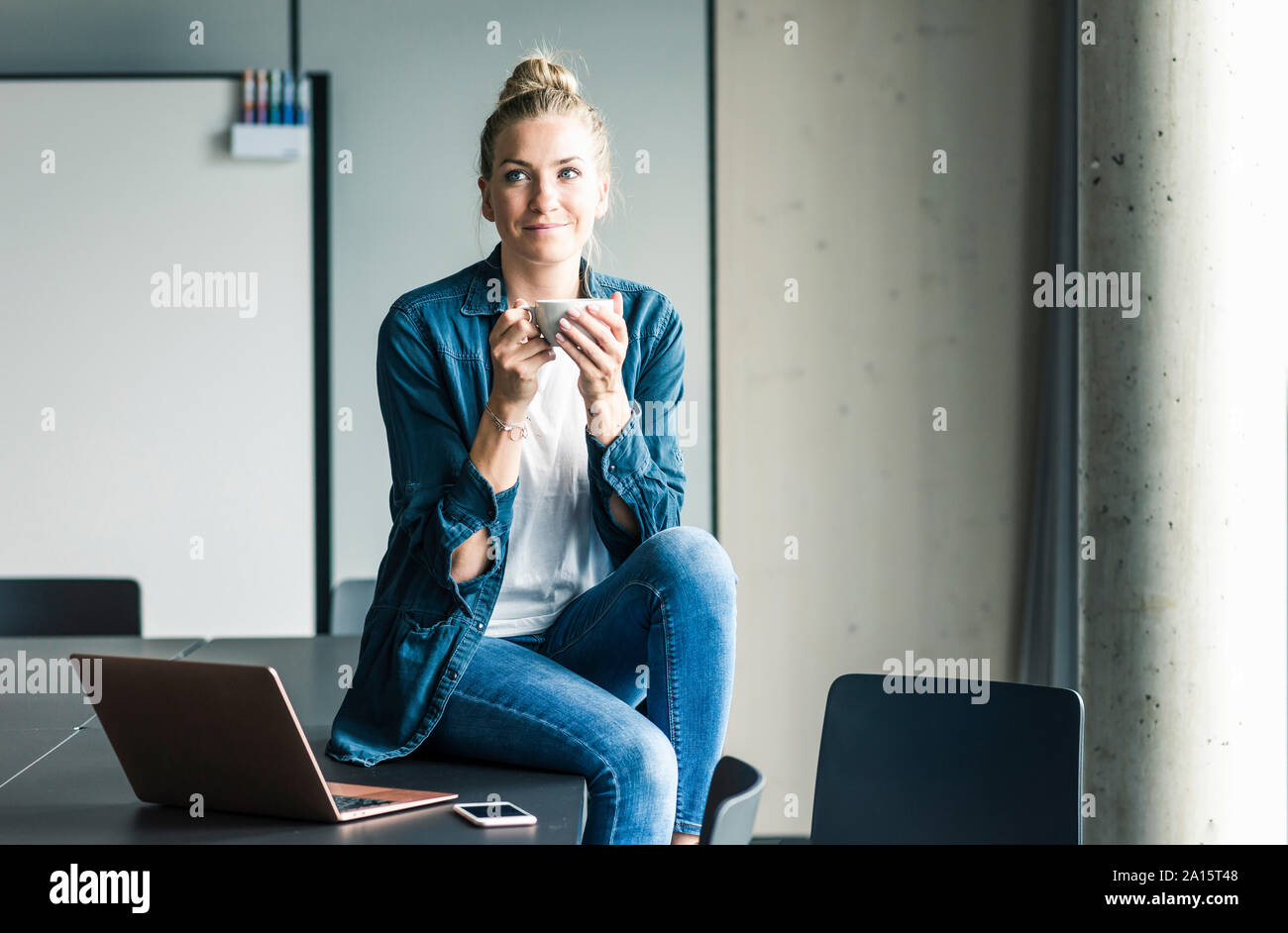 Ritratto di imprenditrice seduta sul tavolo in ufficio avente una pausa caffè Foto Stock