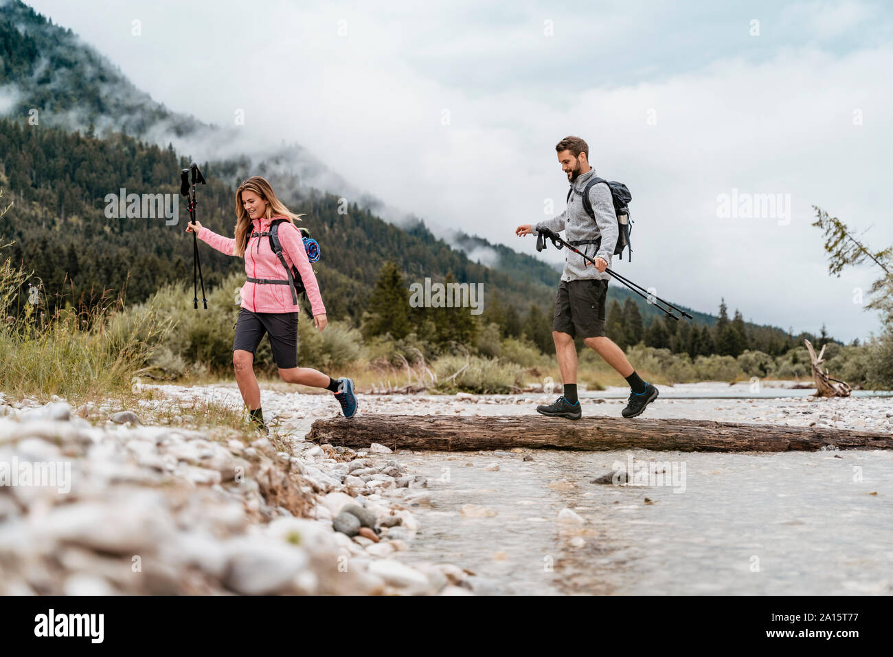 Una giovane coppia in un viaggio escursionistico Varcando il fiume su un registro, Vorderriss, Baviera, Germania Foto Stock