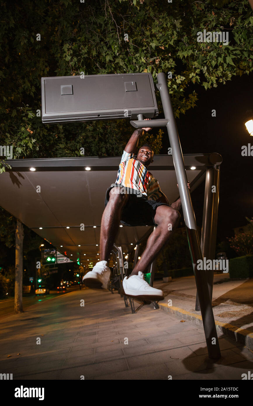 Giocoso giovane uomo appeso su un steet e segno di notte nella città Foto Stock