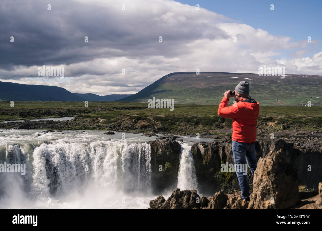 Uomo che guarda le cascate Godafoss, Islanda, con il binocolo Foto Stock