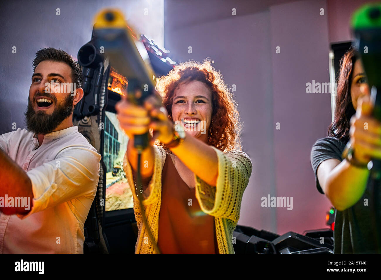 Happy amici a suonare e a sparare con pistole in un divertimento arcade Foto Stock