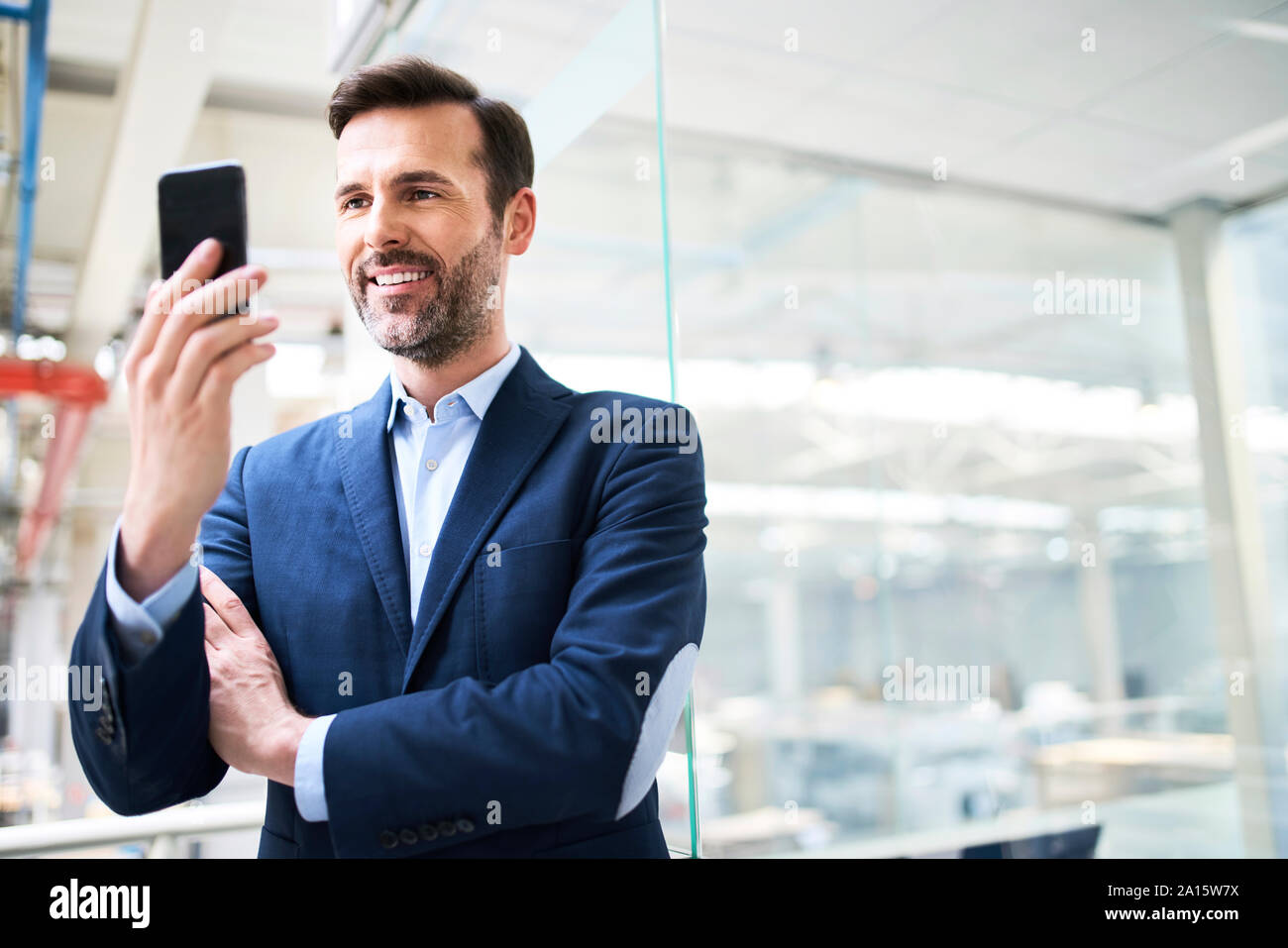 Imprenditore sorridente utilizzando il cellulare in fabbrica Foto Stock