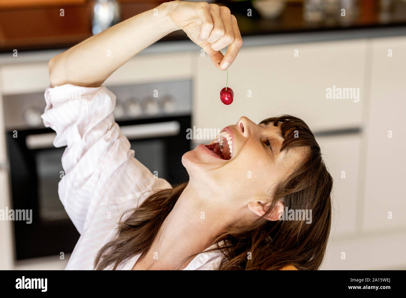 Donna felice di mangiare una ciliegia in cucina a casa Foto Stock