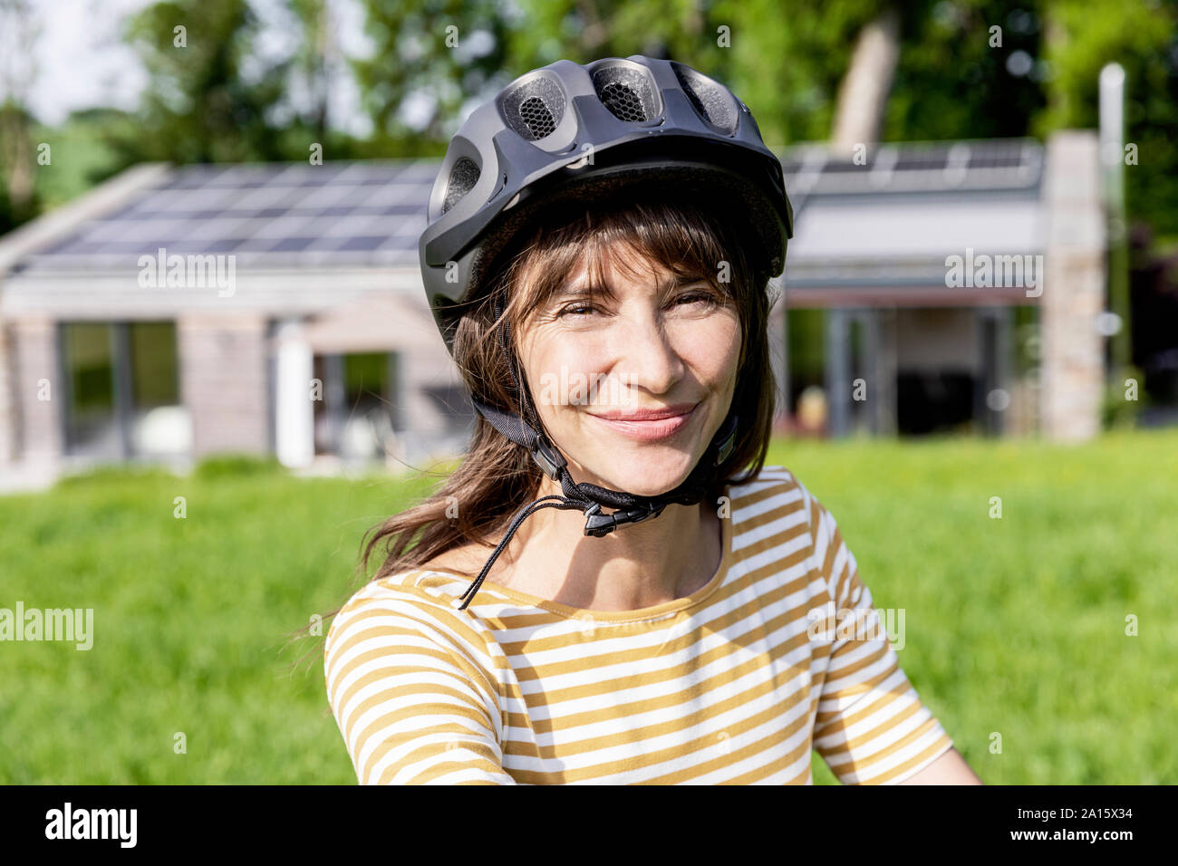 Ritratto di donna sorridente con noleggio casco su un prato di fronte a una casa Foto Stock Ritratto di donna sorridente con noleggio casco su un prato di fronte a una casa Foto Stock