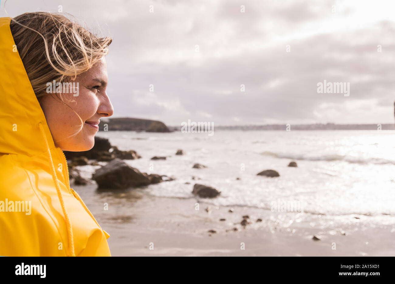Donna che indossa giallo Giacca pioggia in piedi alla spiaggia rocciosa Foto Stock