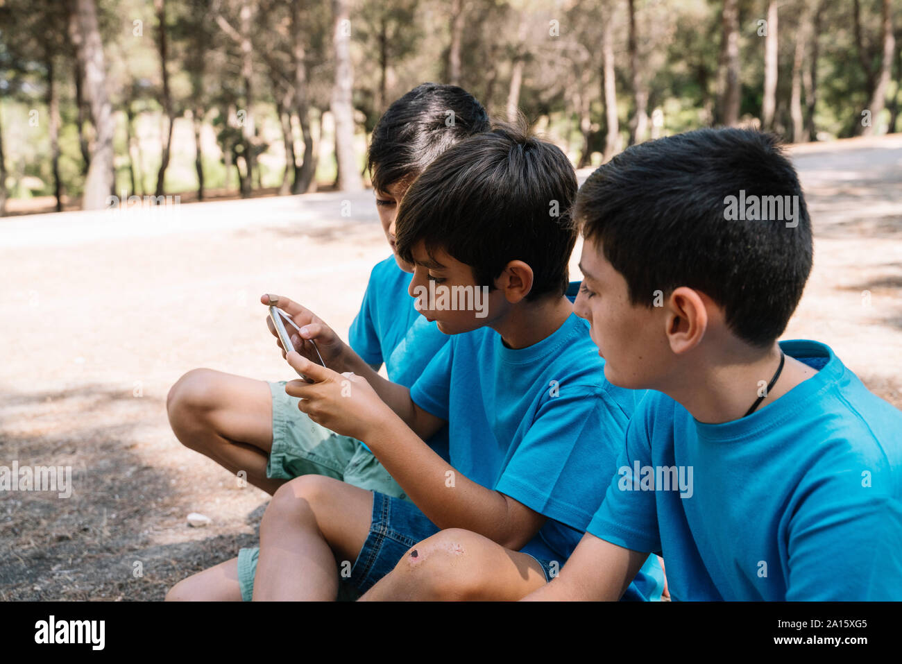 Tre ragazzi in blu t-shirt utilizza lo smartphone Foto Stock