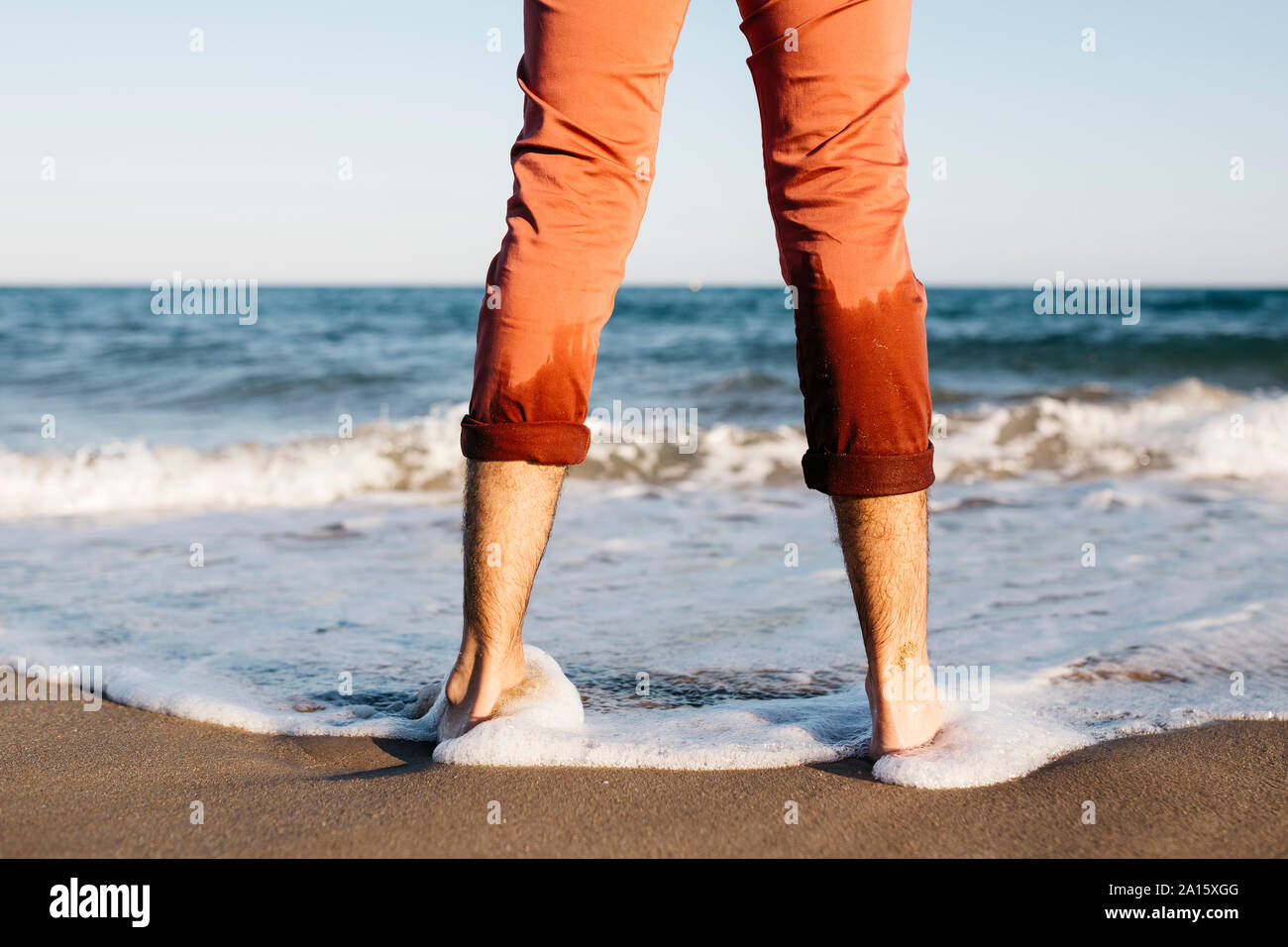 Vista posteriore dell'Uomo con pantaloni arancione in piedi su una spiaggia a bordo d'acqua Foto Stock