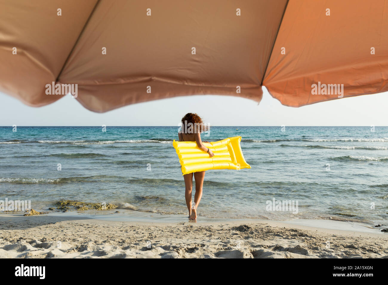 Giovane donna con giallo airbed in spiaggia Foto Stock