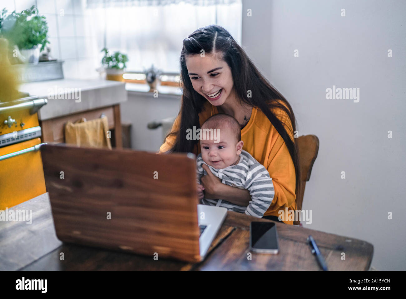 Ridendo madre con bambino con computer portatile sul tavolo da cucina Foto Stock