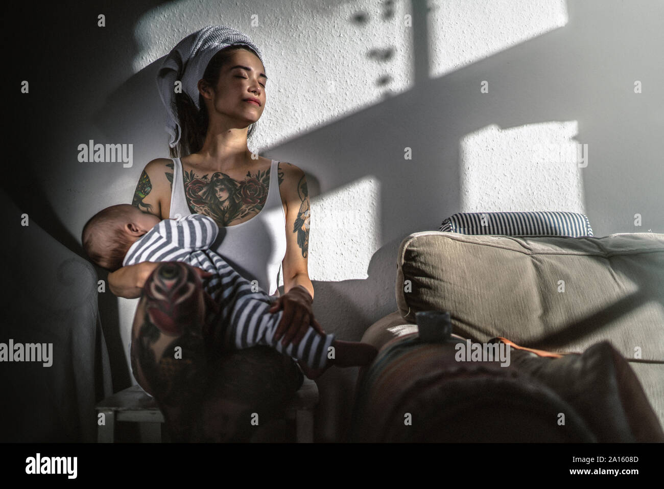 Tatuato giovane donna tenendo il suo bambino a casa godendo il sole Foto Stock