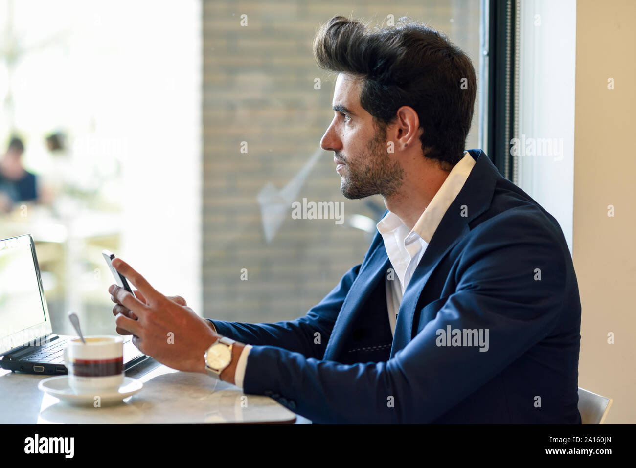 Imprenditore con smartphone e laptop in un ambiente urbano cafe Foto Stock