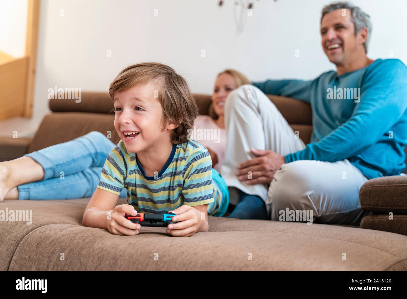 Ragazzo disteso sul lettino a casa la riproduzione del video gioco con i genitori a guardare Foto Stock