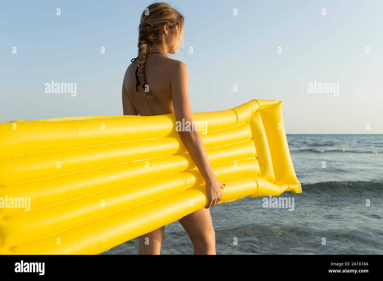 Vista posteriore della giovane donna con giallo airbed in spiaggia, guardando a distanza Foto Stock