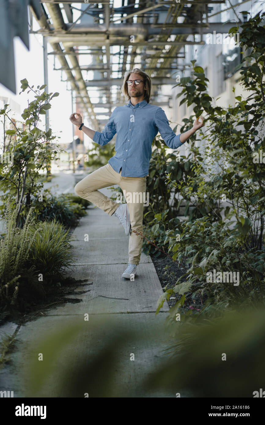 Giovane uomo meditando sul marciapiede circondato da piante Foto Stock