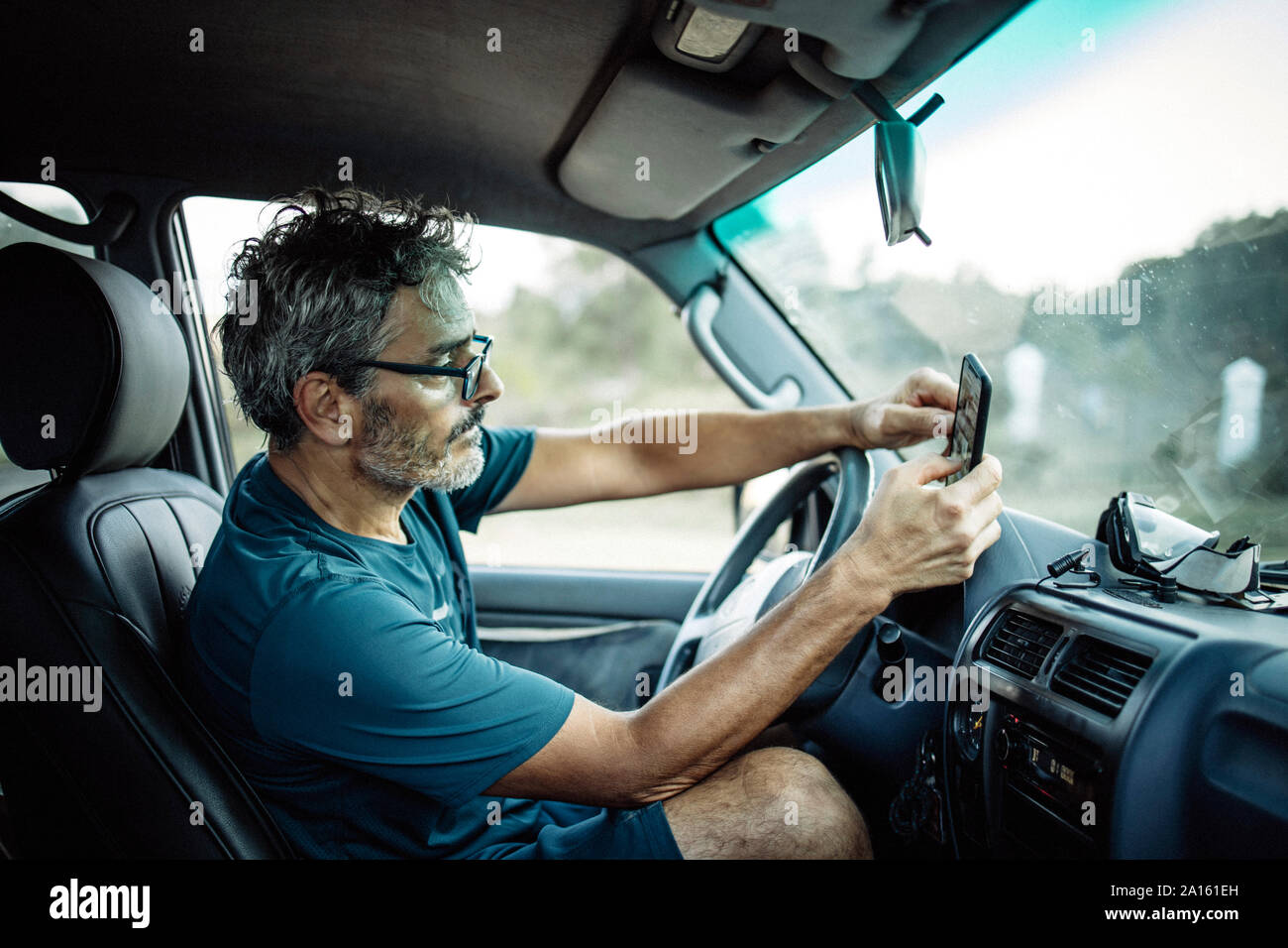 Uomo maturo seduta seduta nel suo veicolo fuoristrada controllare il suo smartphone Foto Stock