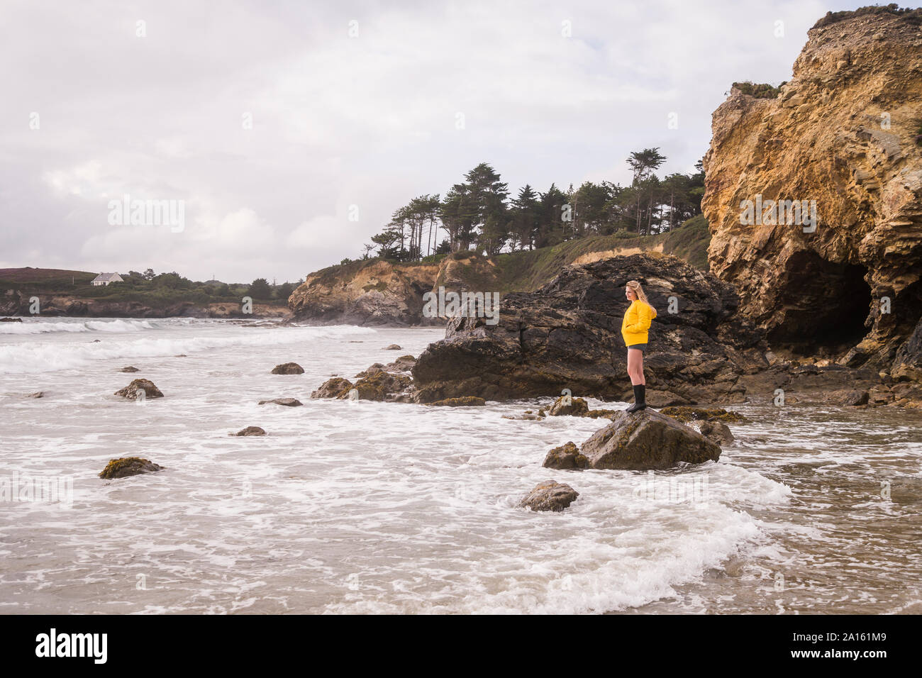 Donna che indossa giallo Giacca pioggia permanente sulla roccia alla spiaggia Foto Stock