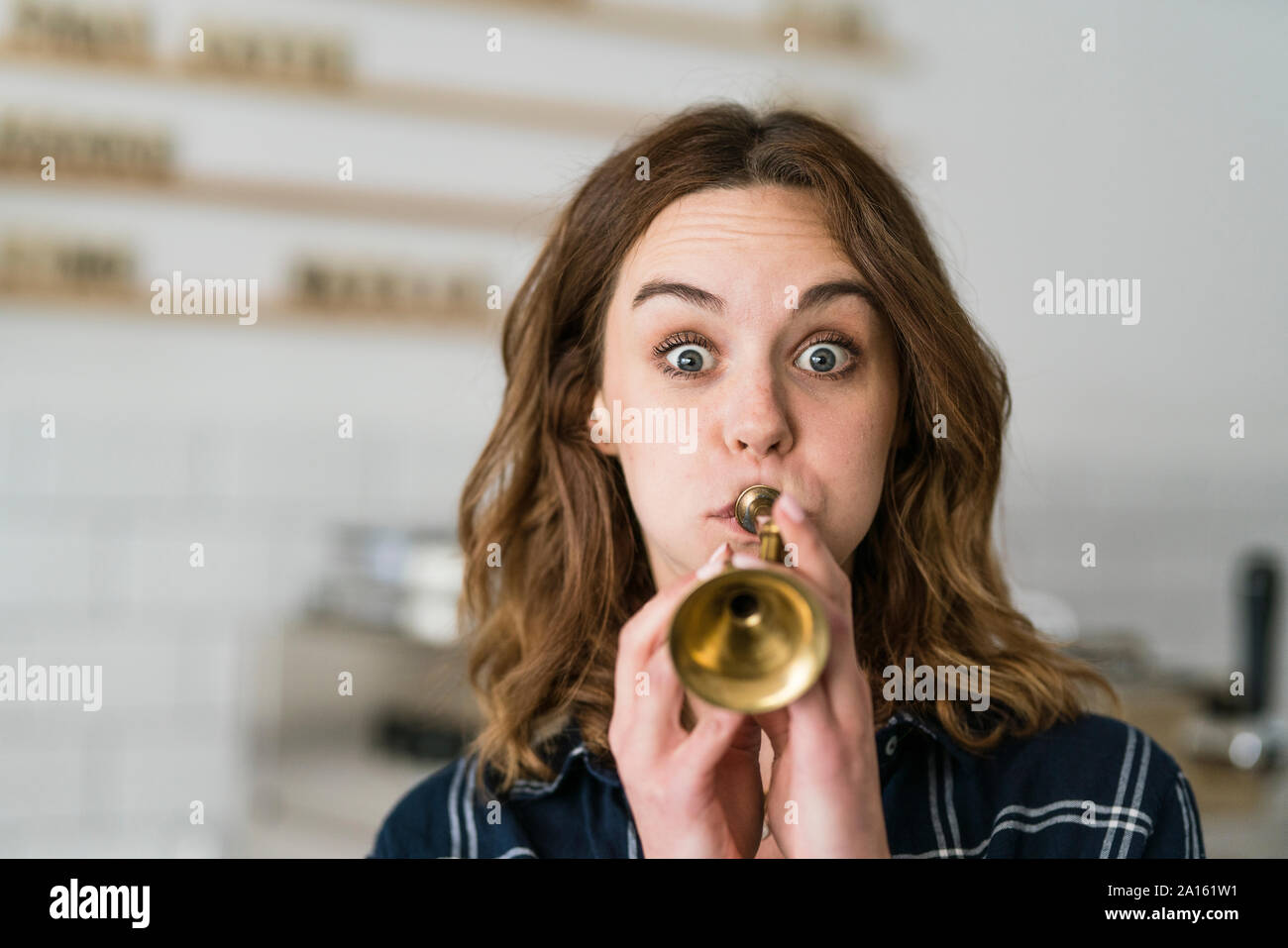 Giovane donna giocattolo di soffiaggio tromba nella sua caffetteria Foto Stock