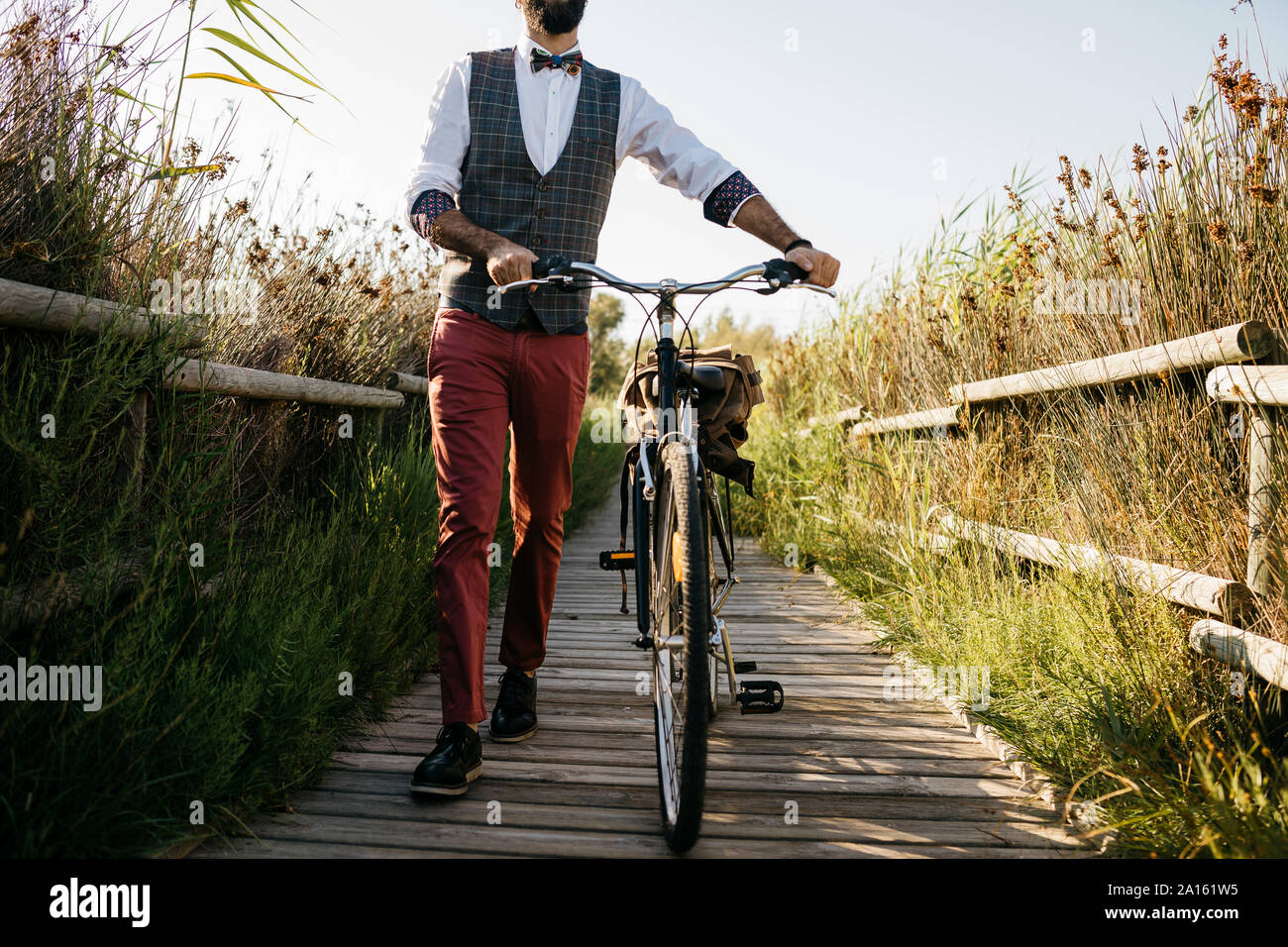 Ben vestito uomo a camminare con la sua bicicletta su una passerella di legno in campagna dopo il lavoro Foto Stock