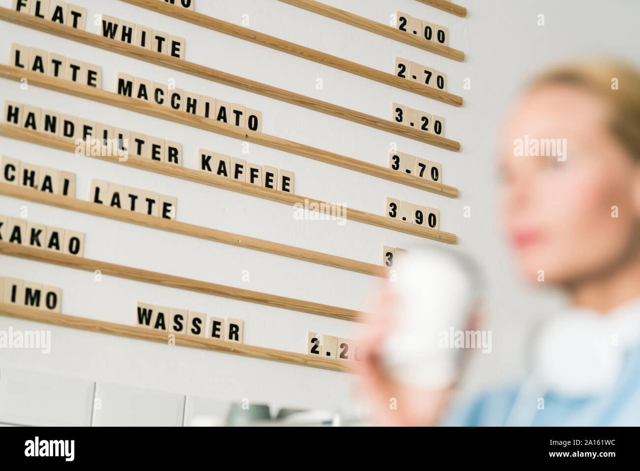 Scheda di prezzo in un caffè con il cliente che porta tazza di caffè Foto Stock