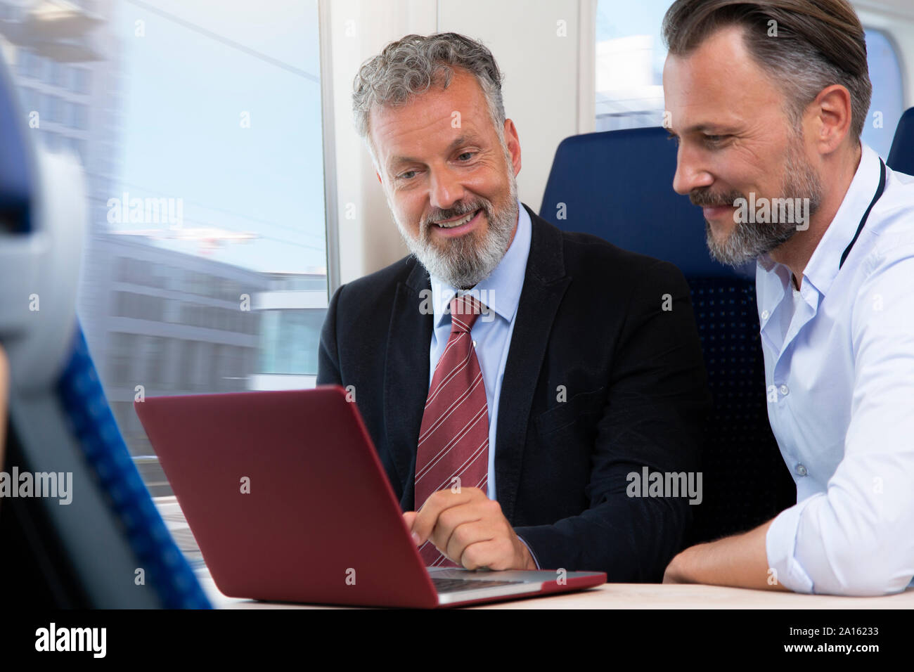 Imprenditori che viaggiano in treno, lavorando sul computer portatile Foto Stock