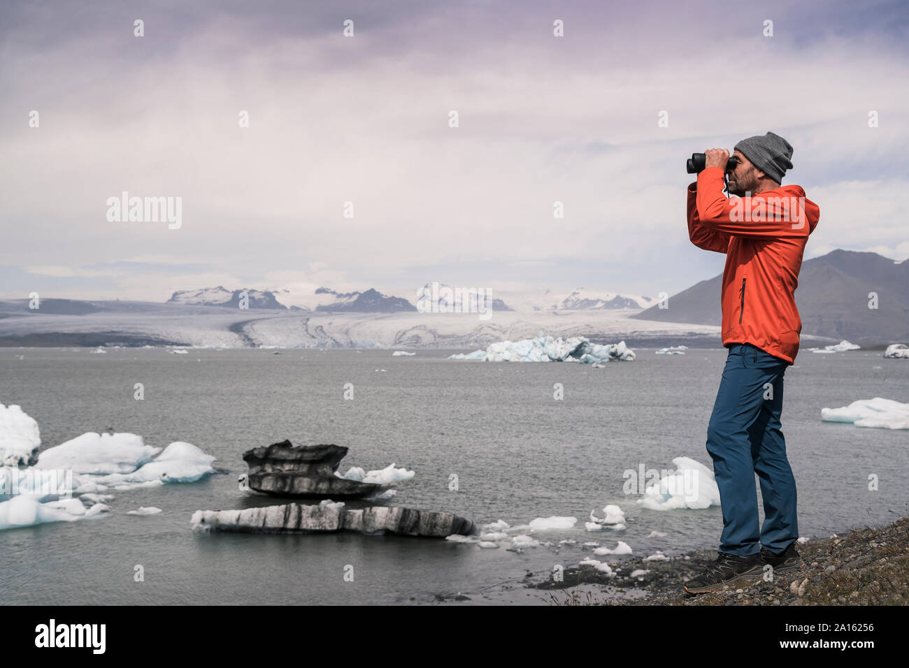 Uomo maturo guardando il ghiacciaio Vatnajokull con il binocolo, Islanda Foto Stock