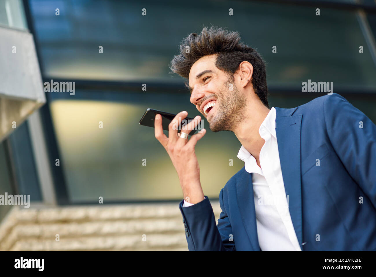 Happy businessman tramite telefono cellulare al di fuori di un edificio per uffici Foto Stock