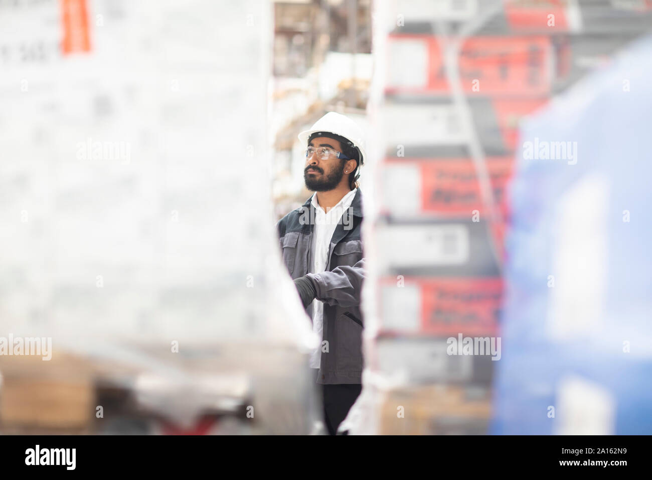 Giovane uomo indossare elmetto lavorando in un magazzino Foto Stock