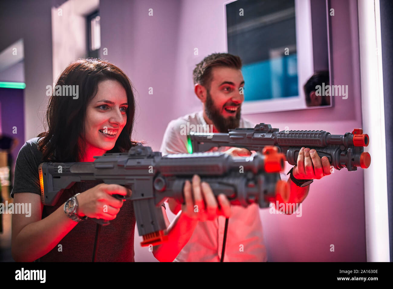 Coppia felice giocando e riprese con i fucili in una sala giochi Foto Stock
