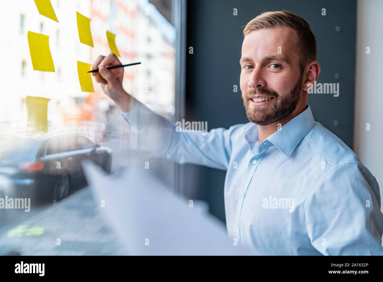 Ritratto di sorridere imprenditore iscritto sulle note di adesivo al pannello in vetro Foto Stock