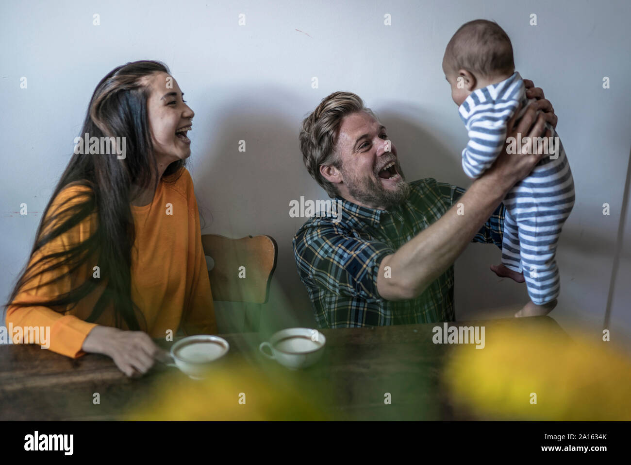 La famiglia felice con il bambino seduto al tavolo di legno a casa Foto Stock