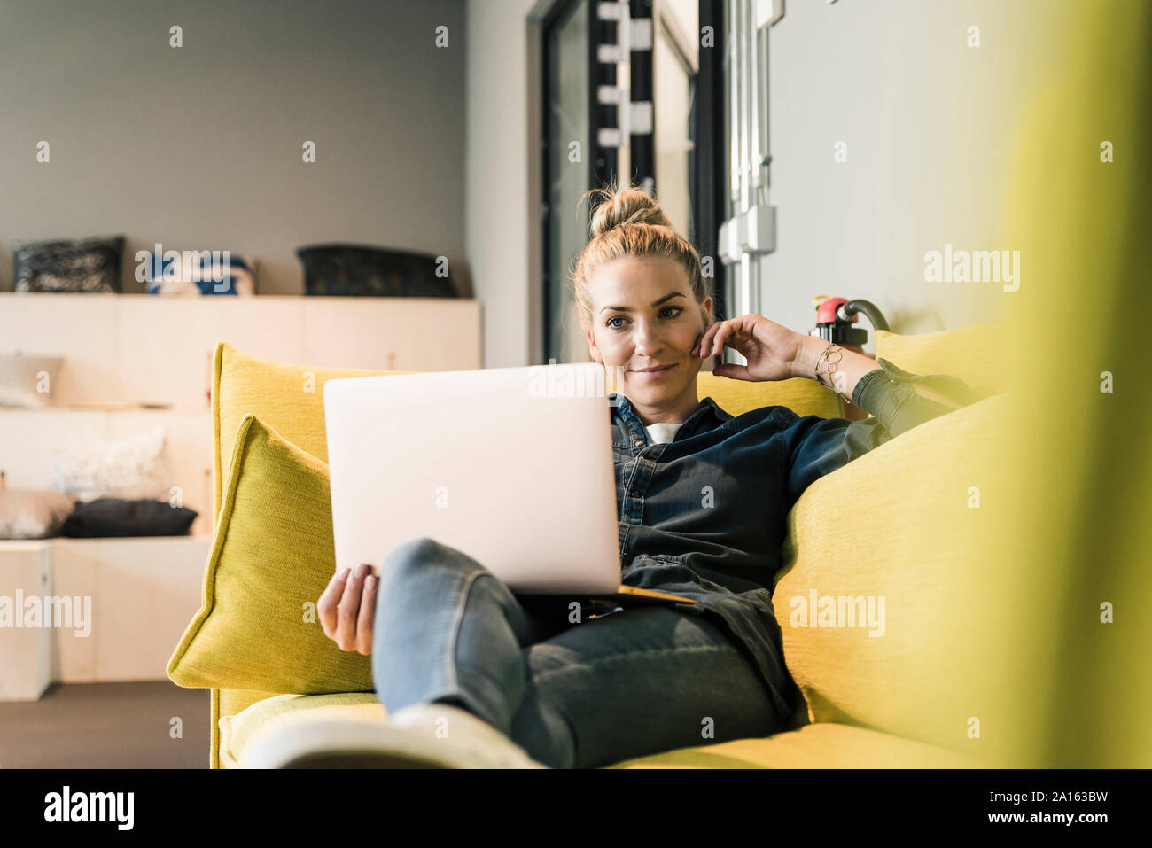 Casual imprenditrice utilizzando laptop sul lettino nella sala di office Foto Stock