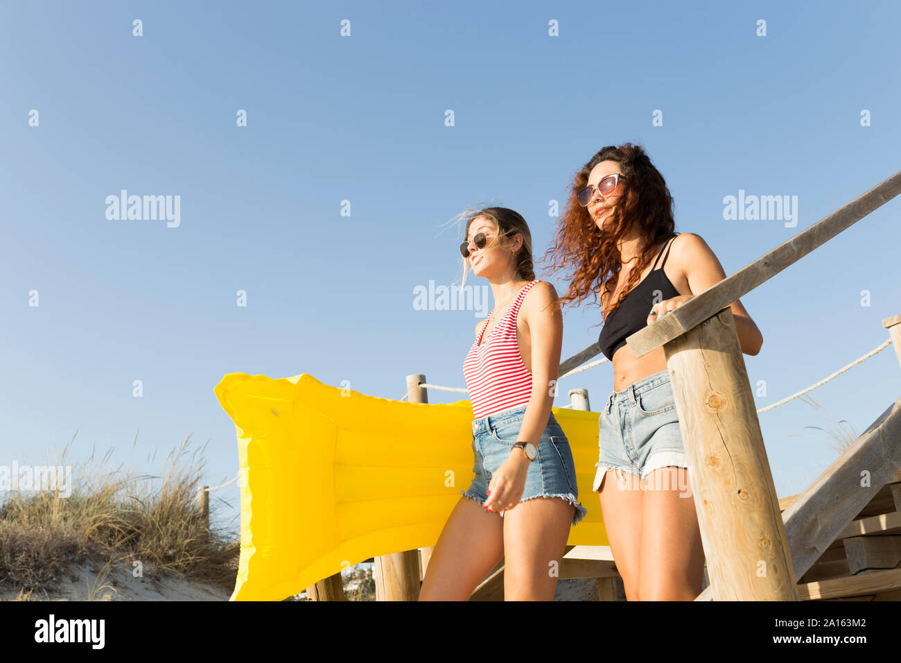 Giovani donne con giallo airbed per raggiungere a piedi la spiaggia Foto Stock